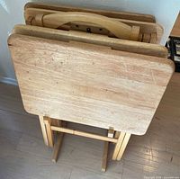 Four folded wooden TV trays in stand