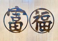 Both metal round wall hangings side by side showing characters and patina