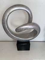 Front view of silver abstract swirl sculpture on black pedestal base