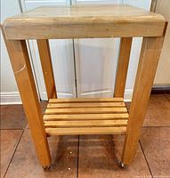 Full view of wooden kitchen cart showing butcher-block top, legs, slatted shelf and casters