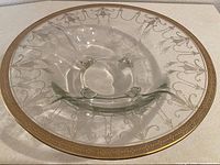 Top view showing entire clear glass bowl, etched pattern, gold rim, and four feet visible through base