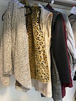 Multiple outerwear pieces hanging: fleece vest, leopard vest, plaid sleeveless jacket, Kenneth Cole plaid jacket, grey puffy jacket partially visible
