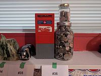 Red Canada Post metal coin bank beside large glass jar filled with silvery coins and small jar on top