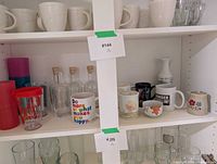 Open cupboard showing plastic tumblers, glass bottles, ceramic mugs and teacups on middle shelf