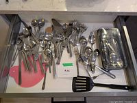Open drawer showing majority of mixed stainless steel flatware and nylon spatula