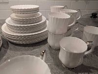 Stacked dinner, salad and bread plates with mugs and cups visible