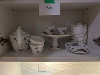 Full set on shelf showing teapot, teacup, cake stand with creamer and sugar, stacks of bowls and plates