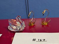 Three swan figurines including one faceted crystal and two amber-accent glass pieces