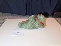 Full view of soapstone seal lying on display base with cedar bark scarf visible