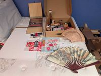 overview of lot on bed showing fans, box of miniatures, framed art, foam board
