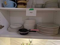Stacked white plates, bowls and two mini fry pans on shelf