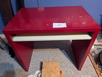Front view of red desk with white pull-out tray extended, showing overall form