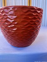 Front and side view of red-orange glazed ceramic planter with textured wave pattern