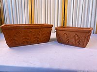 Two terracotta planters side by side showing size difference and exterior pattern