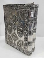 Front and spine view of silver-clad book-form box showing latch and repousse detail