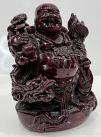 Front view of dark red resin Laughing Buddha statue showing smile, beads, coins, and dragon base
