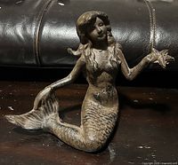 Front three-quarter view of cast iron mermaid figurine with starfish showing overall form and patina