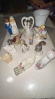 Group shot of all porcelain/ceramic items including figurines, planter, vase, wall pockets, shell