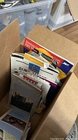 Stack of assorted travel brochures in open cardboard box