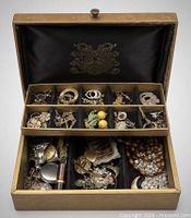 Open box showing internal compartments filled with assorted jewelry and watches