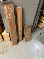 Three black walnut boards leaning vertically, each with chalk-marked dimensions