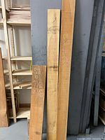 Front view of three rough sawn Douglas Fir boards leaning against shelving, chalk size markings visible