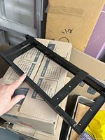 Hand indicating black metal slide frame resting on cardboard box