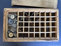 Top view of wooden box showing 24 compartments filled with assorted watch parts