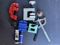 Group shot showing all tools: red pipe cutter, grey press, turquoise magnetizer block, blue case holder, link pin punch, F-clamp, metal weight
