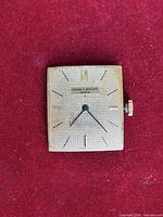 Front view showing square gold-tone textured dial with markers and hands