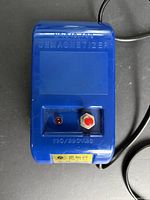 Top view showing blue demagnetizer housing, push button, indicator LED, embossed labeling and attached power cord