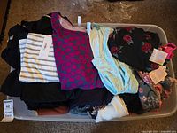 Plastic bin filled with assorted women’s tops showing variety of colours and prints