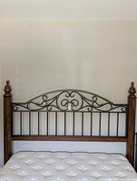 Full view of headboard attached to mattress showing wood posts, metal scrollwork and spindles
