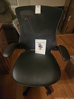 Front view showing mesh back, leather seat, armrests, instruction manual on seat