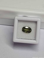 Loose oval green sapphire in small white gem display box, face-up view