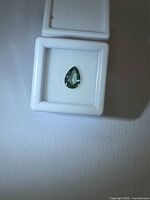 Pear cut aqua blue-green sapphire in white display case, overall view