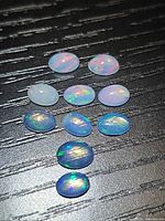 All ten oval opal cabochons arranged on dark background showing play of colour