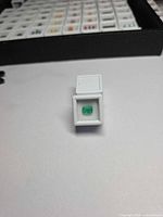 Emerald in display box within tray of other gems