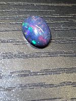 Front view of oval black opal displaying multicoloured play-of-colour