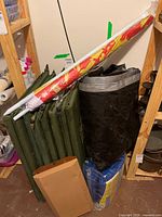 Group view of stacked green inflatable mats, rolled black tarp, blue tarps and red/yellow fabric roll