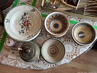 Overview of five bowls and two small lidded pieces on lace cloth