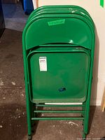 stack of four green folding metal chairs folded