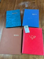 Four closed stamp albums in teal, blue, brown, red