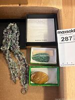 Overview showing all three items in boxes: fluorite necklace, aventurine carving, stone brooch