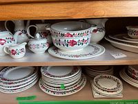 Overview of dinnerware on shelves including serving pieces and stacked plates