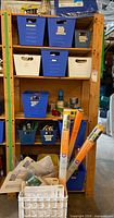 Shelving unit with blue and white bins containing assorted painting tools, Gila window film rolls, application kits, paint rollers and trays visible.