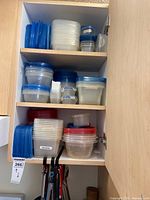 cabinet shelves holding multiple plastic food storage containers with lids plus some utensils below