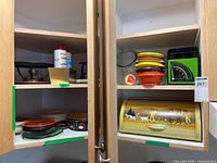 Overall view of cupboard showing breadbox, scale, plastic bowls, fuel, chafing accessories, ceramic bowls