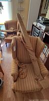 Two striped upholstered wingback chairs with fabric bolt draped, armrest covers on seat