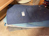 Stack of four chevron-stitched moving blankets showing colors and dirt
